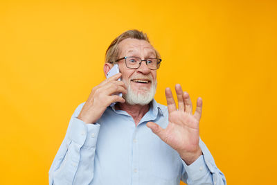 Senior man talking on phone against yellow background