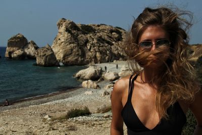 Young woman wearing sunglasses on rock by sea against sky
