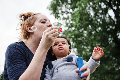 Mother blowing bubbles with son at park