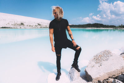 Full length of man standing on rock by lake against sky