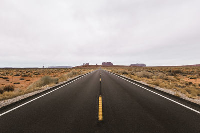 Empty road at desert against cloudy sky