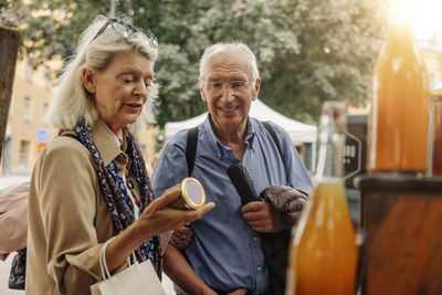 Senior woman examining jar while standing by man at market