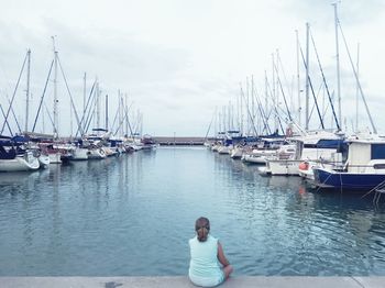 Rear view of woman sitting on pier at harbor