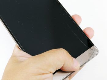 Cropped hand holding broken mobile phone against white background