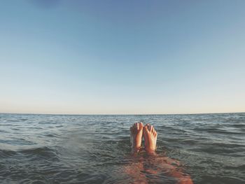 Low section of person in sea against clear sky during sunset