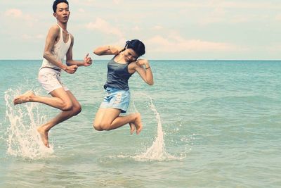 Full length of happy young man jumping in sea against sky