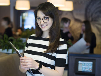 Portrait of confident young woman with clipboard standing in restaurant