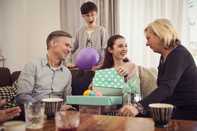 Boy looking at happy sister receiving gifts from grandparents at home