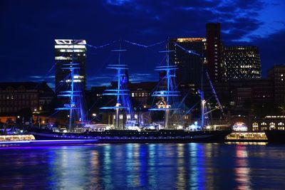 Illuminated city by river against sky