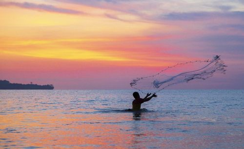 Silhouette of man fishing on beach against dramatic sky