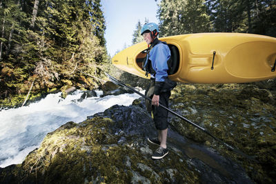 Man carrying kayak while standing by river in forest
