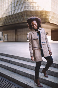 Beautiful african american young woman with afro and large hoop earrings in a stylish coat, smiling
