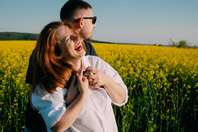 Midsection of woman standing amidst yellow flowering plants on field against sky