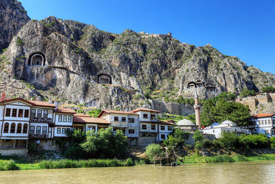 Plants by river and buildings against clear sky