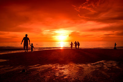 Silhouette men standing on beach against orange sky