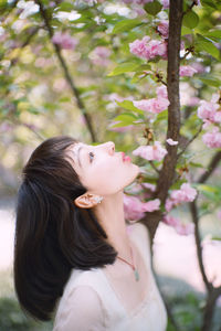 Portrait of woman with pink flower against trees