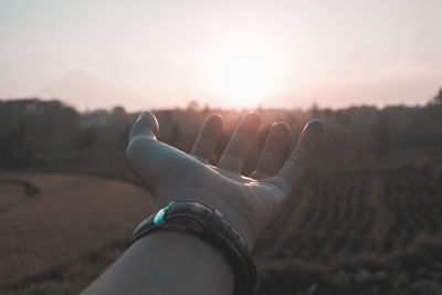 Cropped image of hand wearing wristwatch during sunset