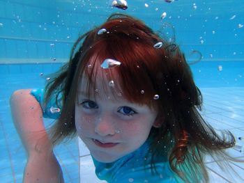 Close-up portrait of cute girl swimming underwater in pool