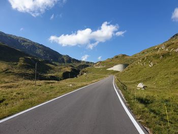 Empty road leading towards mountains against sky