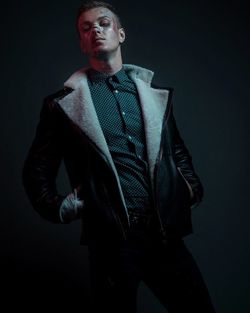 Male model wearing leather jacket while posing against black background