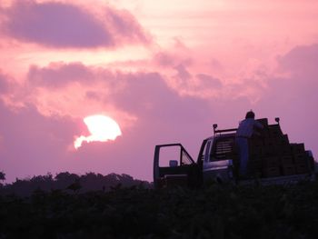 Silhouette man standing on off-road vehicle against cloudy sky during sunset