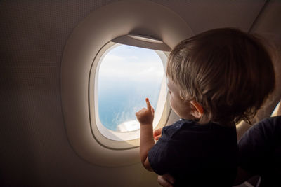 Rear view of boy looking through airplane window