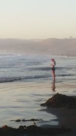 Man standing on beach against sky during sunset