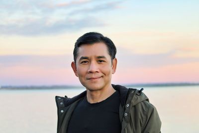 Portrait of young man standing at beach against sky during sunset