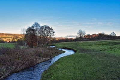 Scenic view of river amidst field against sky during sunset