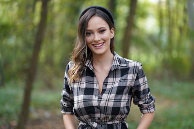 Portrait of smiling young woman standing against trees