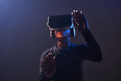 African american female in modern vr headset standing on black background with raised hands while exploring virtual reality in studio