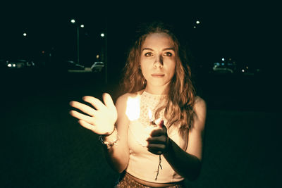 Portrait of young woman holding illuminated light at night