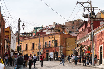 People walking on street amidst buildings in city against sky