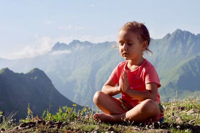 Girl meditating while sitting on mountain against sky