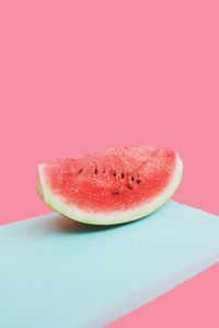 Close-up of watermelon slice on cutting board against pink background