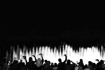 Crowd photographing by fountains against clear sky at night