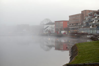 River by buildings against sky during foggy weather