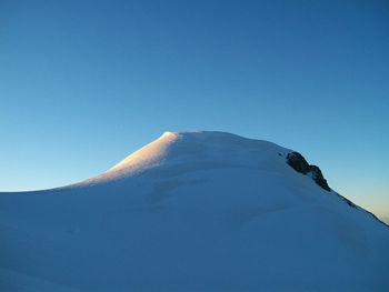 Low angle view of snowcapped mountain against clear blue sky