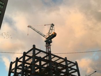 Low angle view of crane at construction site against sky