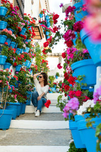 Beautiful woman sitting on a ladder full of pots and flowers in an andalusian patio