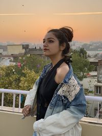 Beautiful woman standing by railing against sunset