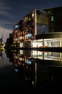 Illuminated buildings by lake against sky in city at night