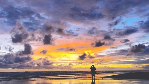 Silhouette woman standing on beach against sky during sunset