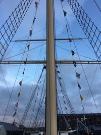 Low angle view of ships mast and rigging against cloudy sky