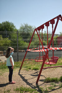 Full length of girl wearing mask standing on playground against sky