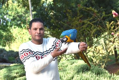 Portrait of man holding macaw in park