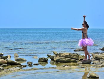 Young woman standing on rock at beach against sky