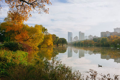 Scenic view of lake by buildings against sky during autumn