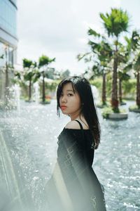 Beautiful young woman standing by tree against sky