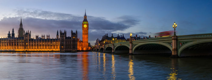 Illuminated bridge over river against sky in city